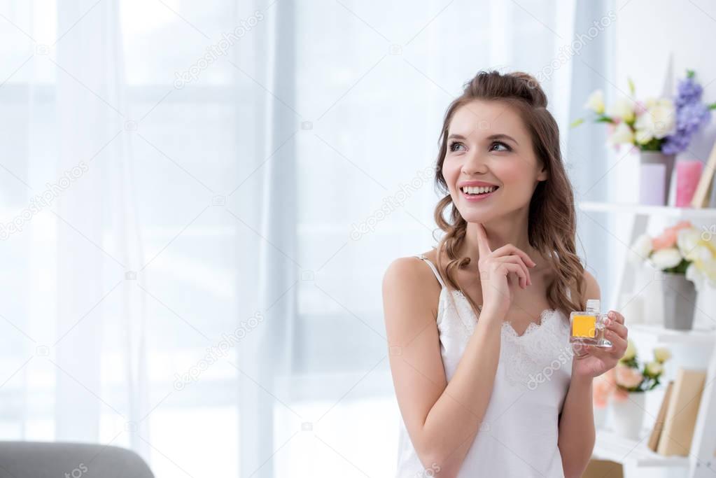 beautiful smiling young woman in lingerie holding bottle of perfume and looking away