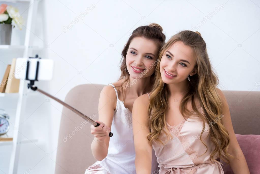 beautiful happy girlfriends taking selfie with smartphone at pajama party
