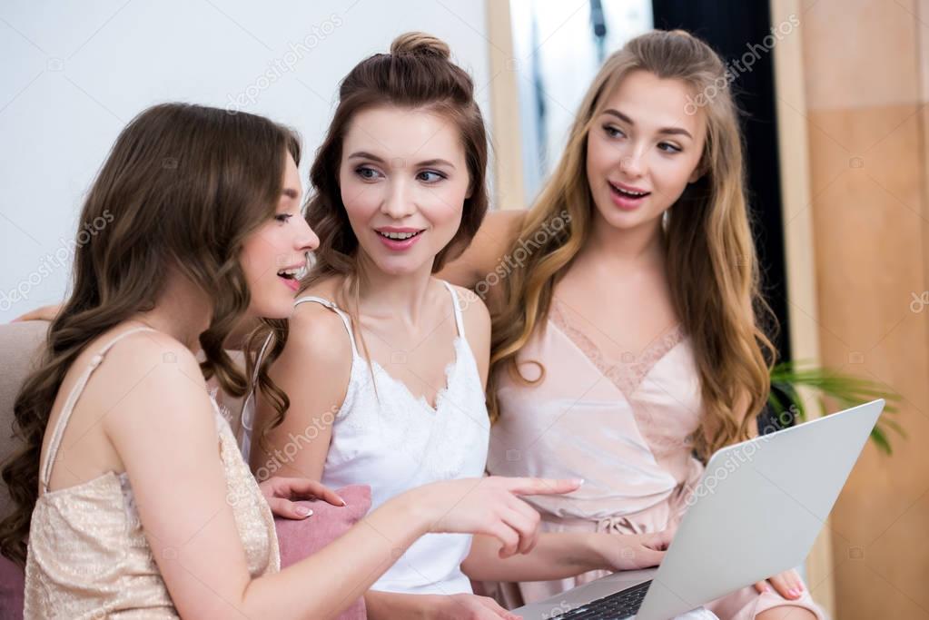 beautiful smiling young women in pajamas using laptop together