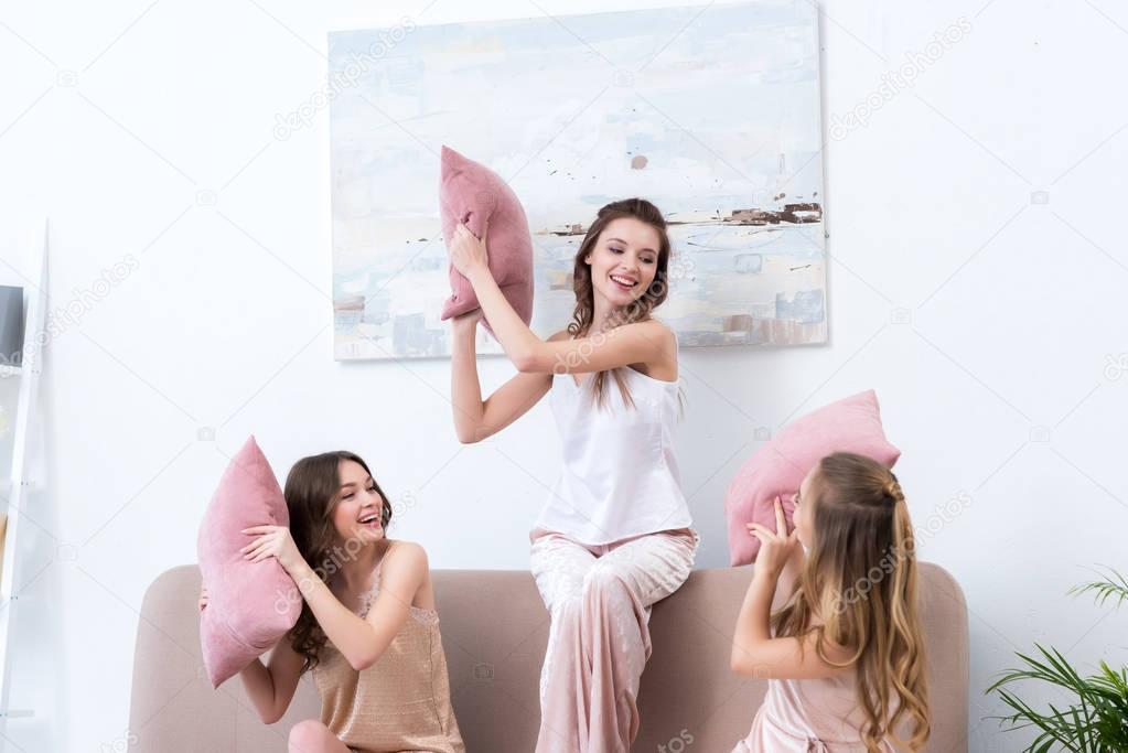 beautiful happy girlfriends in pajamas fighting with pillows at home  