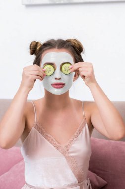 Salatalık dilimleri yüz maskesi ile yakın tutan pijama içinde çekici genç kadın