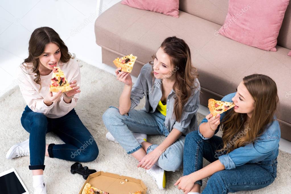 high angle view of beautiful smiling young women eating pizza and talking at home