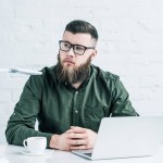 Portrait of thoughtful businessman sitting at workplace with cup of coffee and laptop