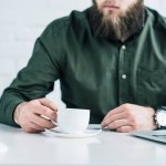 Cropped shot of businessman with cup of coffee at workplace