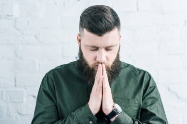 portrait of stylish bearded man praying against white brick wall clipart