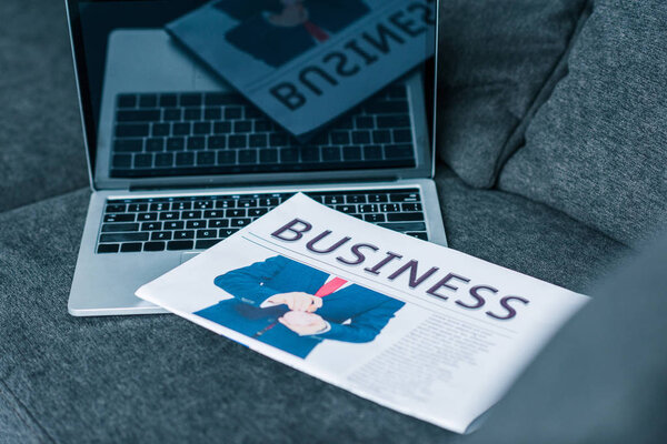 close up view of business newspaper and laptop with blank screen on sofa