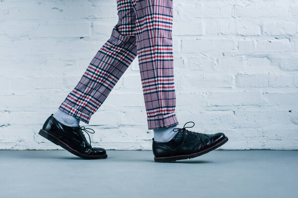 cropped shot of man in stylish shoes walking against white brick wall