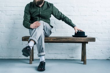 Beyaz duvara karşı şapka ile tahta bankta oturan işadamı kısmi görünümü