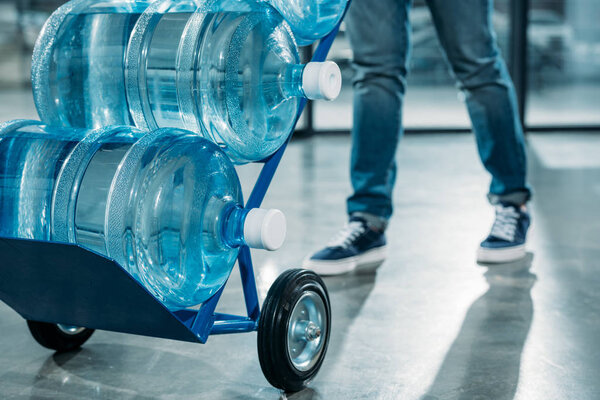 Close-up view of loader man pushing cart with water bottles