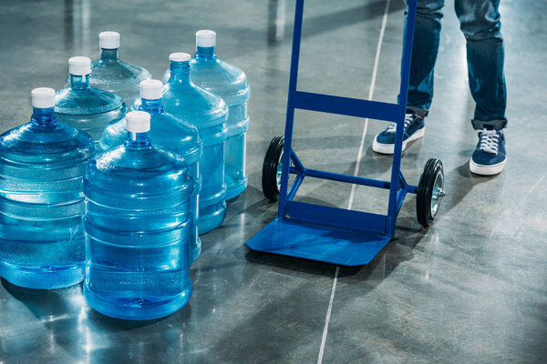 Courier with delivery cart standing by water bottles