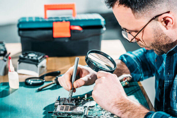Hardware engineer looking at circuit board through magnifying glass