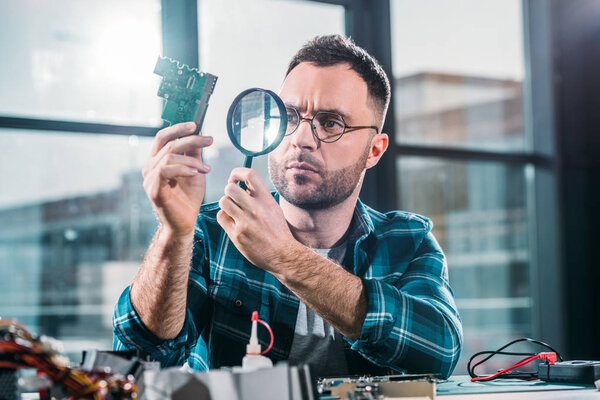 Hardware engineer looking at circuit board through magnifying glass