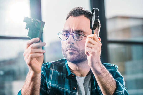 Engineer holding circuit board and magnifying glass