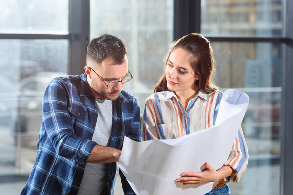 Female and male engineers looking at blueprint and discussing project
