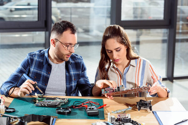 Man assisting woman in circuit board repair