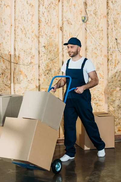 Loader man carrying cardboard boxes on hand truck