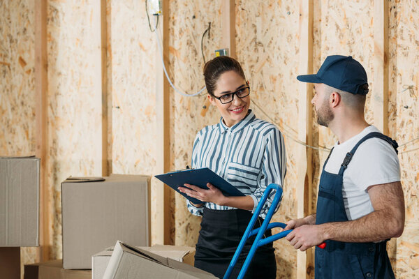 Delivery man and businesswoman filling checklist by stacks of boxes