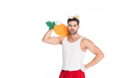 Man with bunny ears holding big carrot on shoulder isolated on white, easter concept