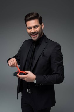 Şık adam izole çözmeyi şerit üzerinde hediye kutusu gri, uluslararası kadın gün kavramı üzerinde gülümseyen