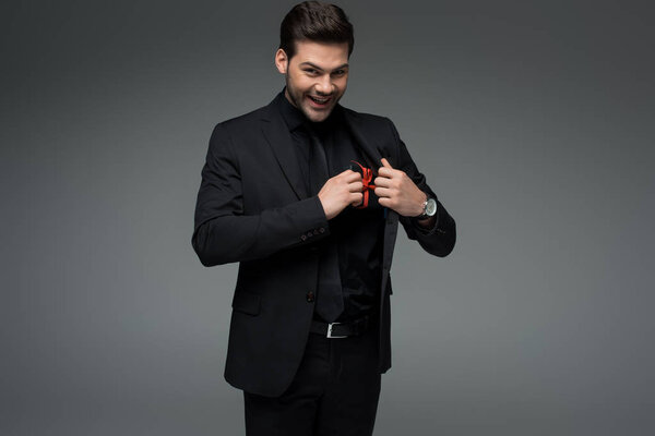 Young male putting gift box in pocket of jacket isolated on grey, international womens day concept