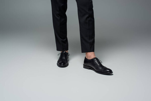 Partial view of stylish male legs in black formal shoes on grey
