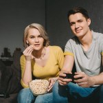 Подружка ест попкорн и смотрит, как бойфренд играет в видеоигры дома Подружка ест попкорн и смотрит, как бойфренд играет в видеоигры дома