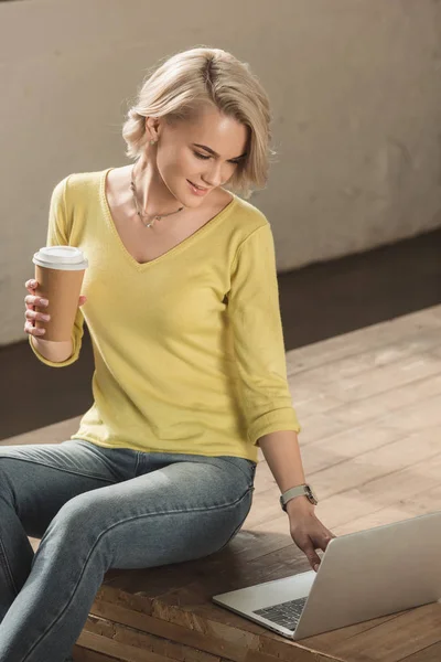 紙コップでコーヒーを保持して 自宅のラップトップを使用して魅力的な女の子  — 無料ストックフォト