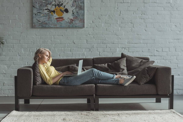 side view of beautiful girl lying with laptop on sofa