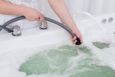cropped shot of spa salon assistant regulating water in hydro bath clipart