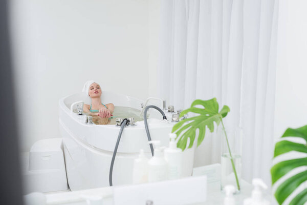 молодая женщина в купальнике с полотенцем на голове расслабляющий в ванне в спа-салоне
