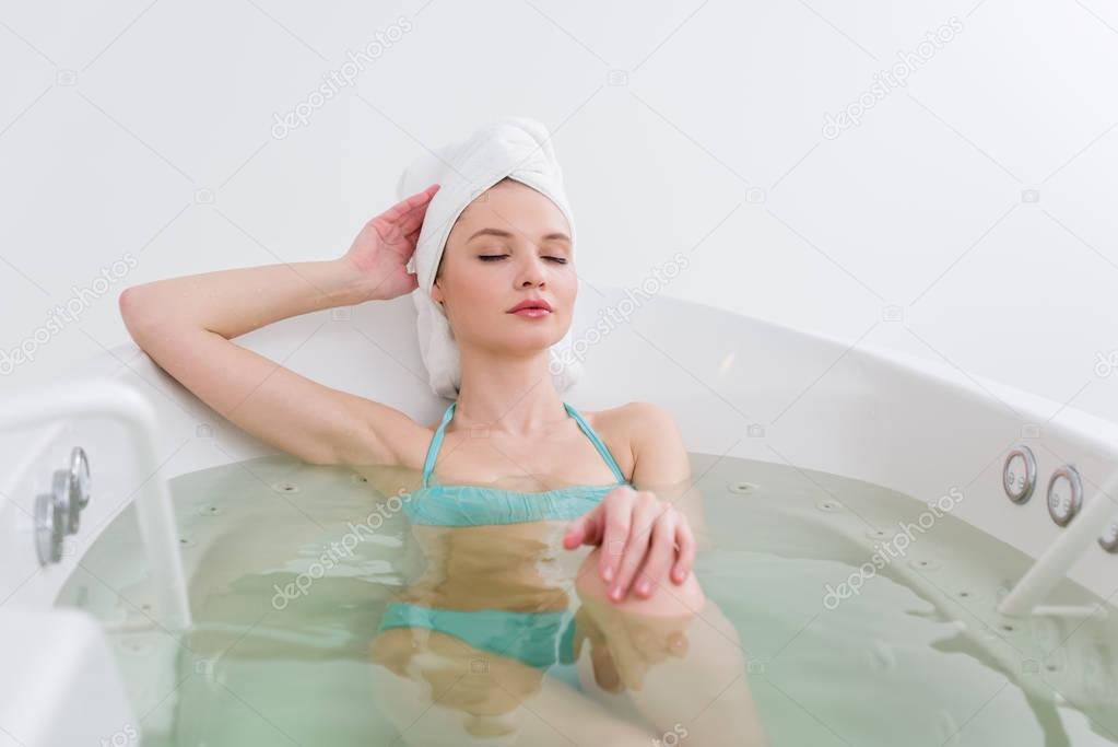 portrait of woman in swimming suit with towel on head relaxing in bath in spa salon
