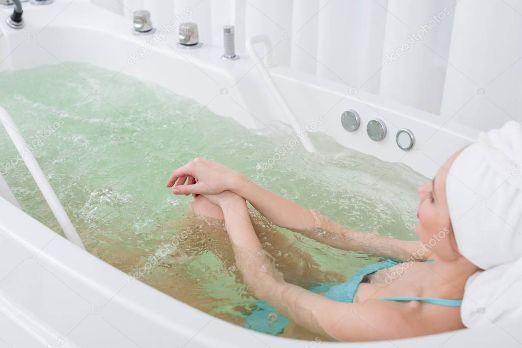 side view of woman in swimming suit with towel on head relaxing in bath in spa salon