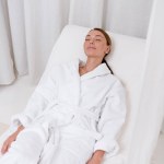 Mujer atractiva joven en albornoz blanco con los ojos cerrados descansando en el salón de spa