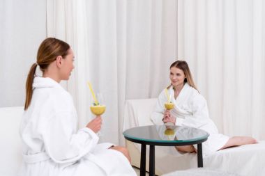 genç kadınlarda spa salonda masada oturan kokteyller ile beyaz bornoz