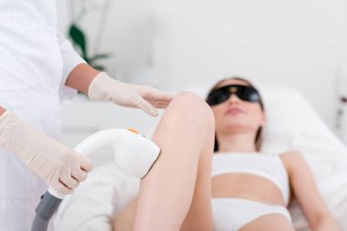 partial view of woman receiving laser hair removal epilation on leg in salon clipart