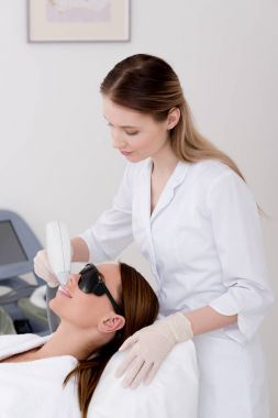 young woman getting laser hair removal procedure on face in salon clipart