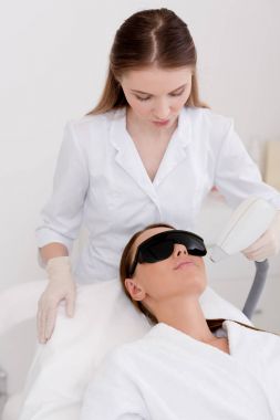 young woman getting laser hair removal procedure on face in salon clipart