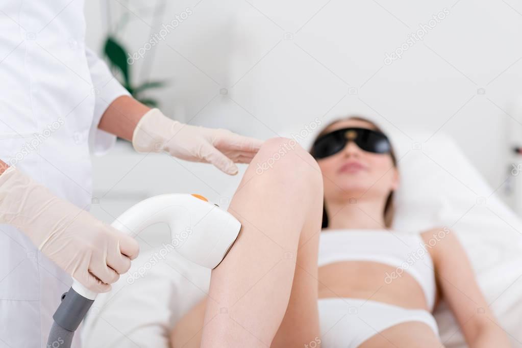 partial view of woman receiving laser hair removal epilation on leg in salon