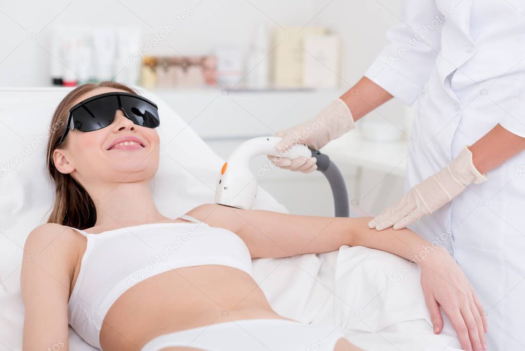 cropped shot of woman getting laser hair removal procedure on arm in salon