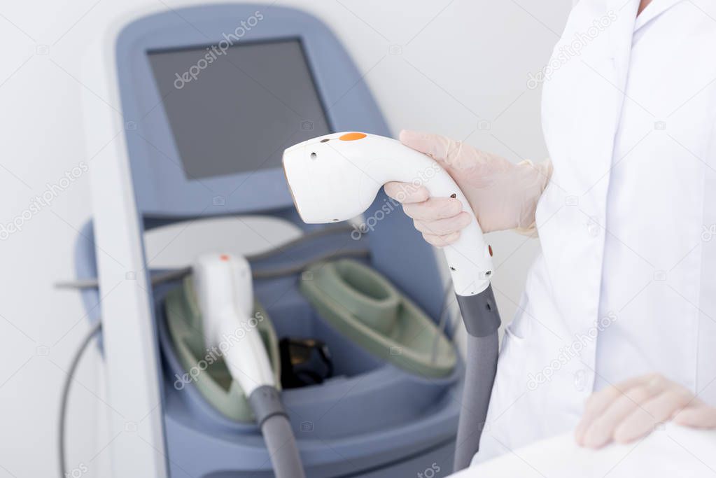 cropped shot of cosmetologist with laser hair removal apparatus in salon