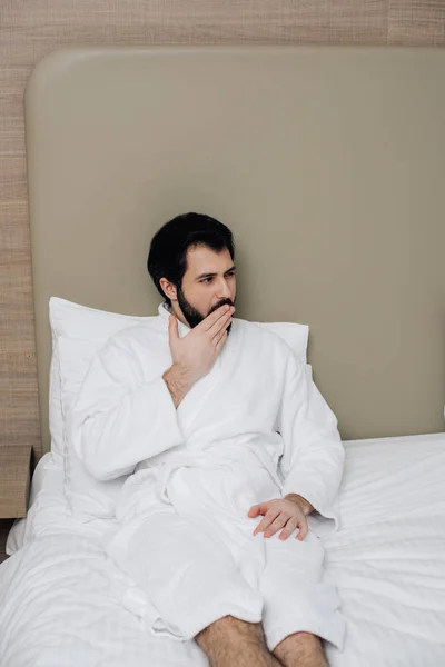 Handsome Man Bathrobe Sitting Bed Hotel Suite Yawning — Stock Photo, Image