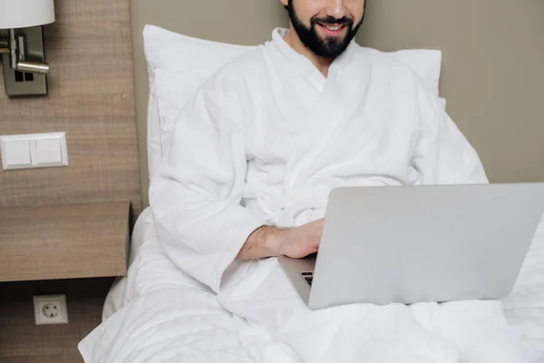 Обрезанный Снимок Улыбающегося Мужчины Халате Ноутбуком Постели Номере Отеля — Бесплатное стоковое фото