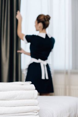 Perdenin ön plan üzerinde duran temiz havlu yığını ile kapatma üniformalı genç hizmetçi