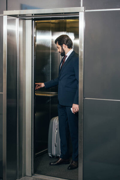 бизнесмен с багажом нажатием кнопки внутри лифта
