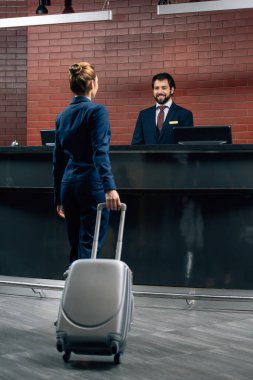 businesswoman with luggage going at hotel reception counter clipart