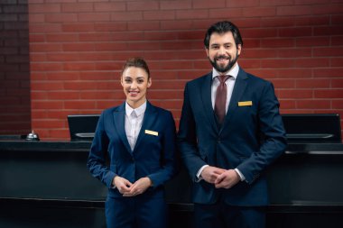 hotel receptionists standing together in front of counter and looking at camera clipart