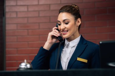 young beautiful hotel receptionist receiving call at workplace clipart