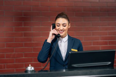 young beautiful hotel receptionist receiving call at workplace clipart