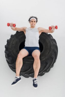 İnce sporcu lastik tekerleğin üzerinde beyaz izole içinde dumbbells ile egzersiz görünümünü yüksek açı