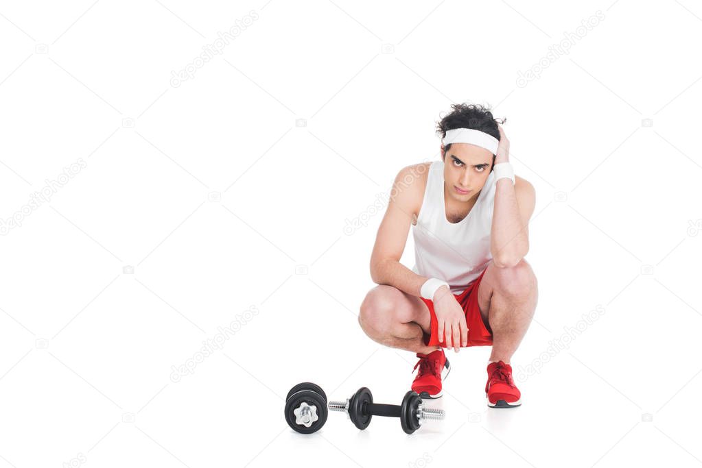 Young skinny man in sportswear sitting near dumbbells